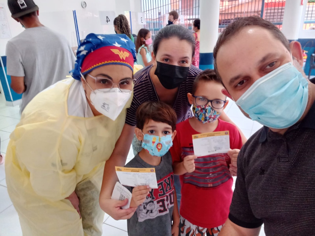 Na imagem está Luiz Artur com os dois filhos segurando a carteirinha de vacinação, a enfermeira e a esposa dele.